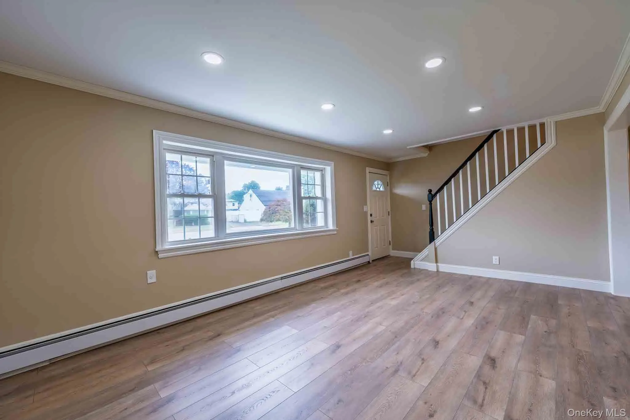 Recessed ceiling lighting, wood-finish flooring, staircase with white risers and dark wood handrail, multiple window panes, and crown molding Recessed ceiling lighting, wood-finish flooring, staircase with white risers and dark wood handrail, multiple window panes, and crown molding