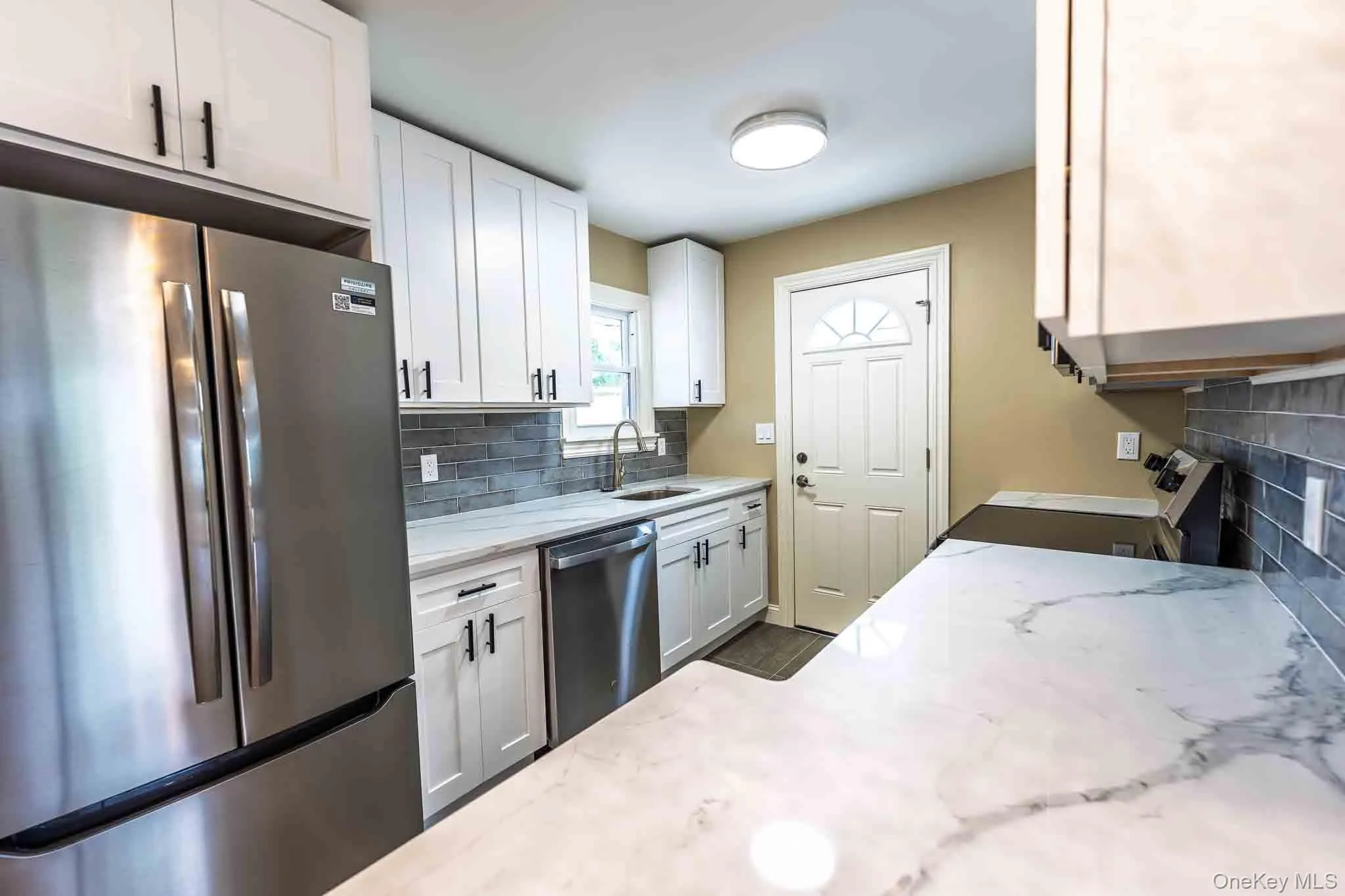 White shaker cabinetry, stainless steel appliances, marble-look countertops, and a gray subway tile backsplash White shaker cabinetry, stainless steel appliances, marble-look countertops, and a gray subway tile backsplash