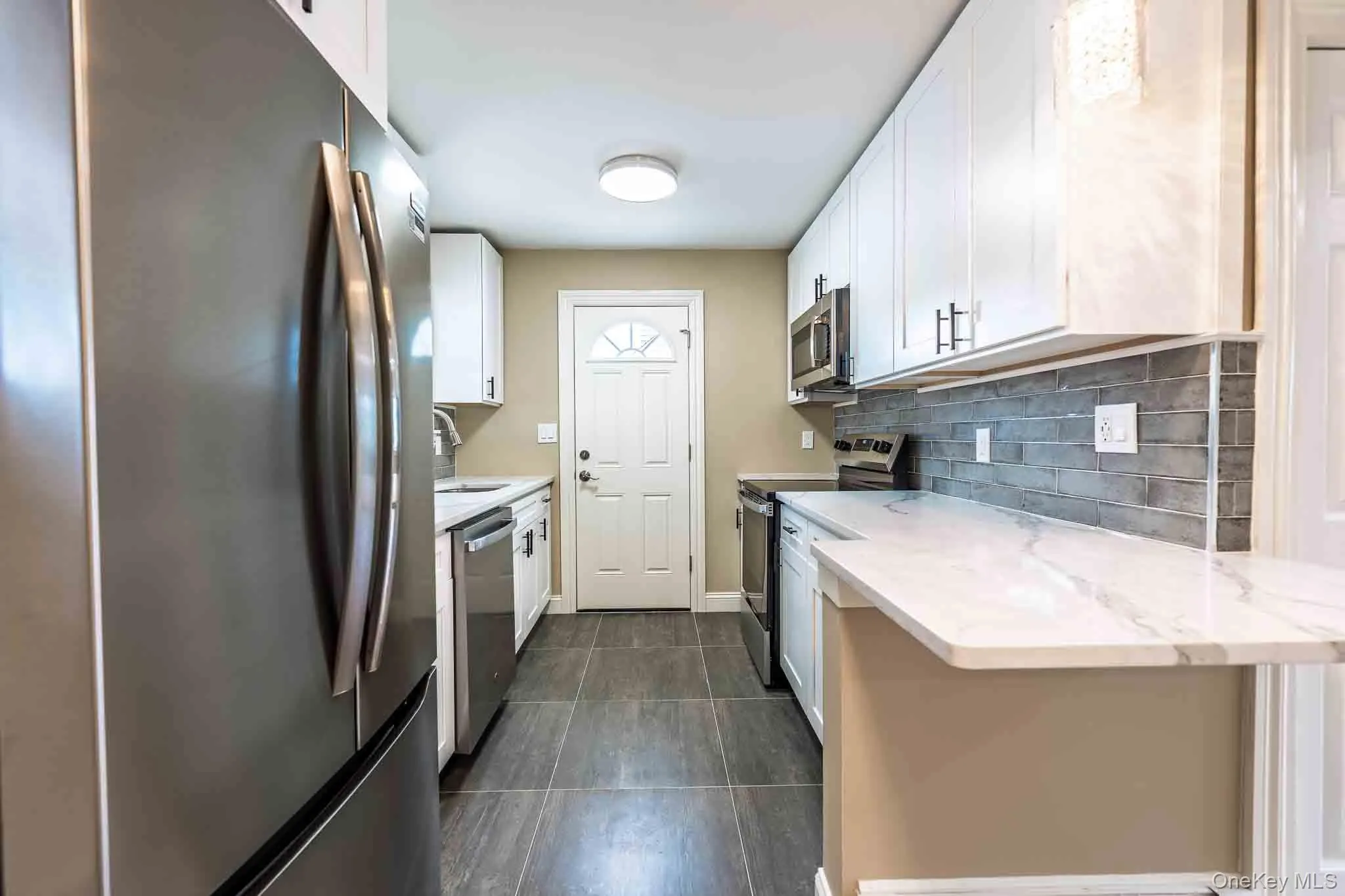 New Galley kitchen with white cabinetry, stainless steel appliances, marble-look countertops, and a gray subway tile backsplash New Galley kitchen with white cabinetry, stainless steel appliances, marble-look countertops, and a gray subway tile backsplash