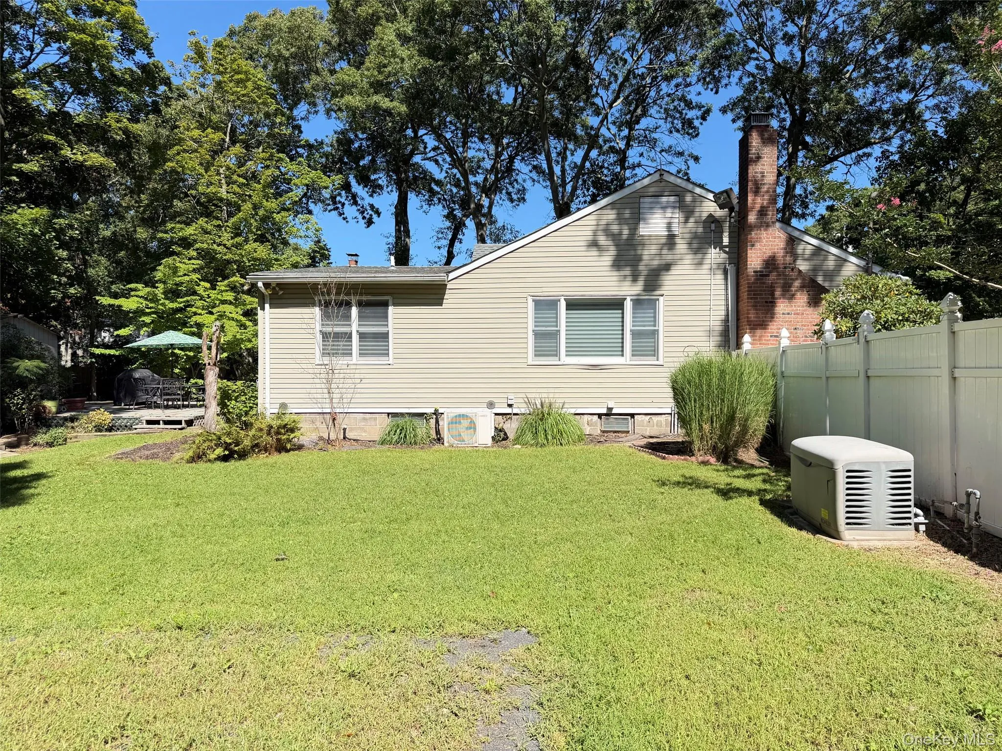 Expansive grassy yard with mature trees, a raised wooden deck, a brick chimney, and vinyl privacy fencing viewing side of structure Expansive grassy yard with mature trees, a raised wooden deck, a brick chimney, and vinyl privacy fencing viewing side of structure