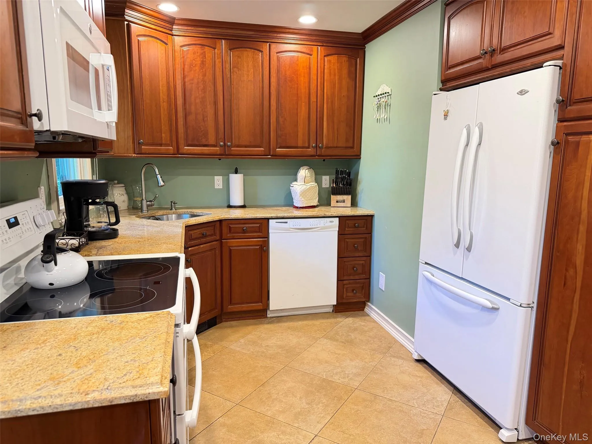 Kitchen with wood cabinetry, light-toned countertops, tile flooring, and white appliances including a built-in microwave, dishwasher, and refrigerator Kitchen with wood cabinetry, light-toned countertops, tile flooring, and white appliances including a built-in microwave, dishwasher, and refrigerator