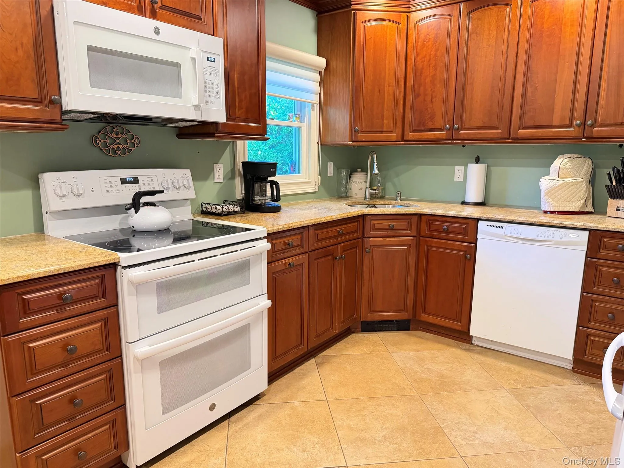 Full kitchen featuring wood cabinetry, light-toned countertops, tiled flooring, an electric range with double ovens, and an over-range microwave Full kitchen featuring wood cabinetry, light-toned countertops, tiled flooring, an electric range with double ovens, and an over-range microwave