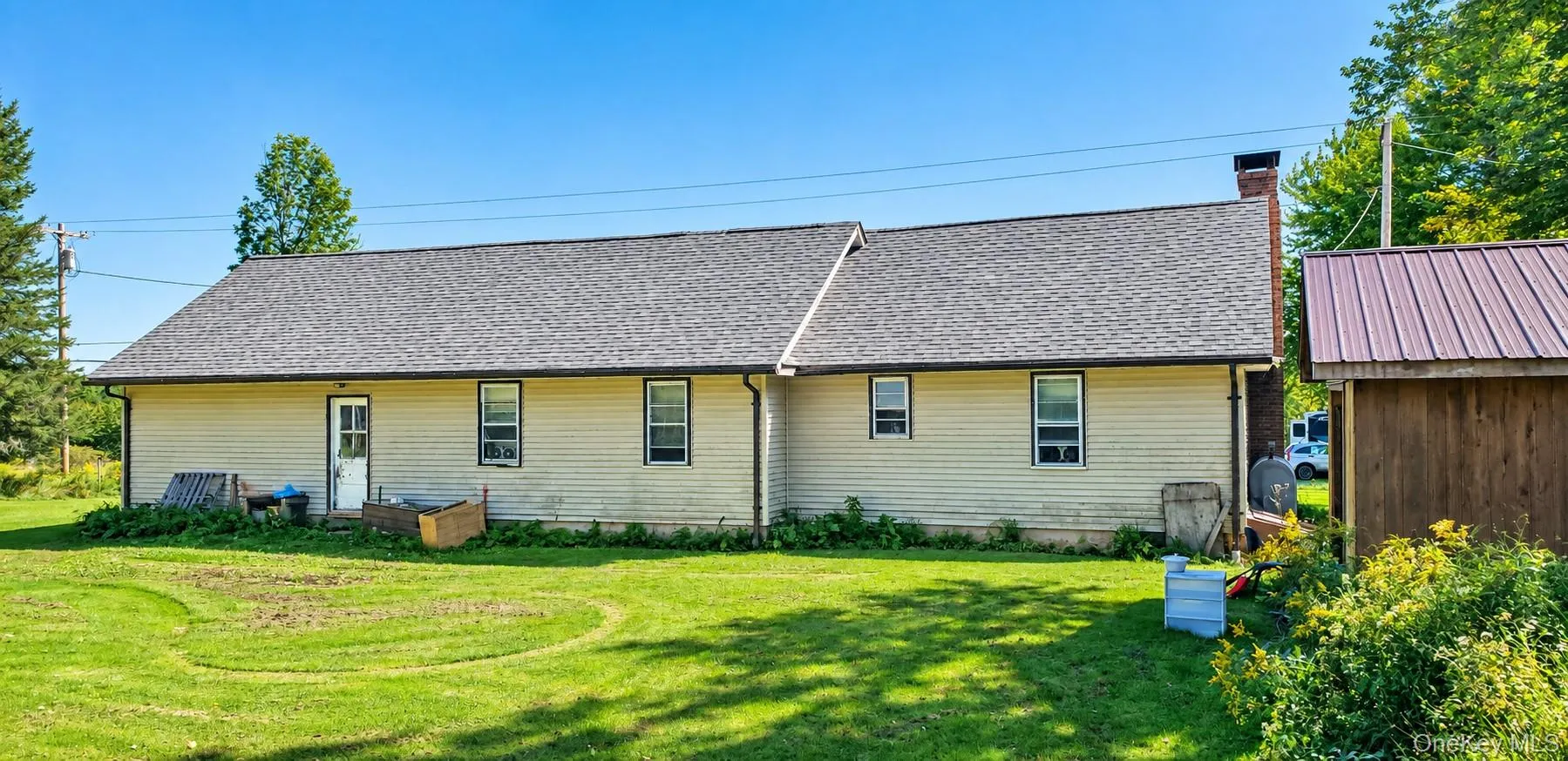 Expansive green lawn with a shingled roofline, vinyl siding, and a detached storage shed with a metal roof Expansive green lawn with a shingled roofline, vinyl siding, and a detached storage shed with a metal roof