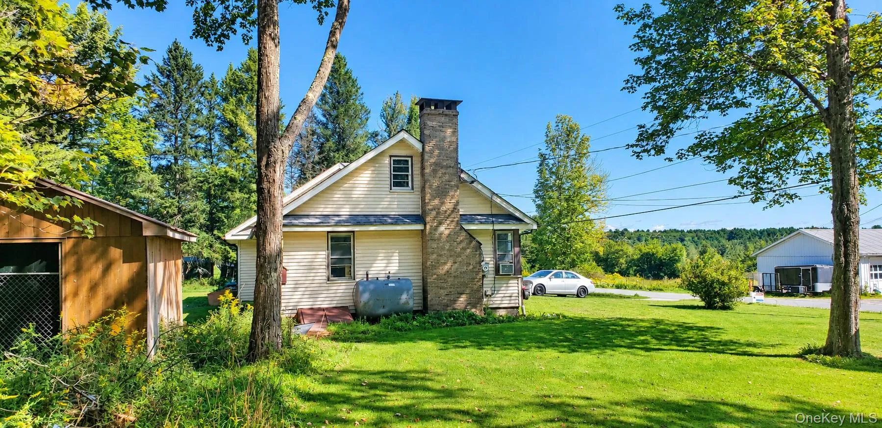 Cream-colored siding exterior, stone-clad chimney, multiple windows, and a detached outbuilding Cream-colored siding exterior, stone-clad chimney, multiple windows, and a detached outbuilding