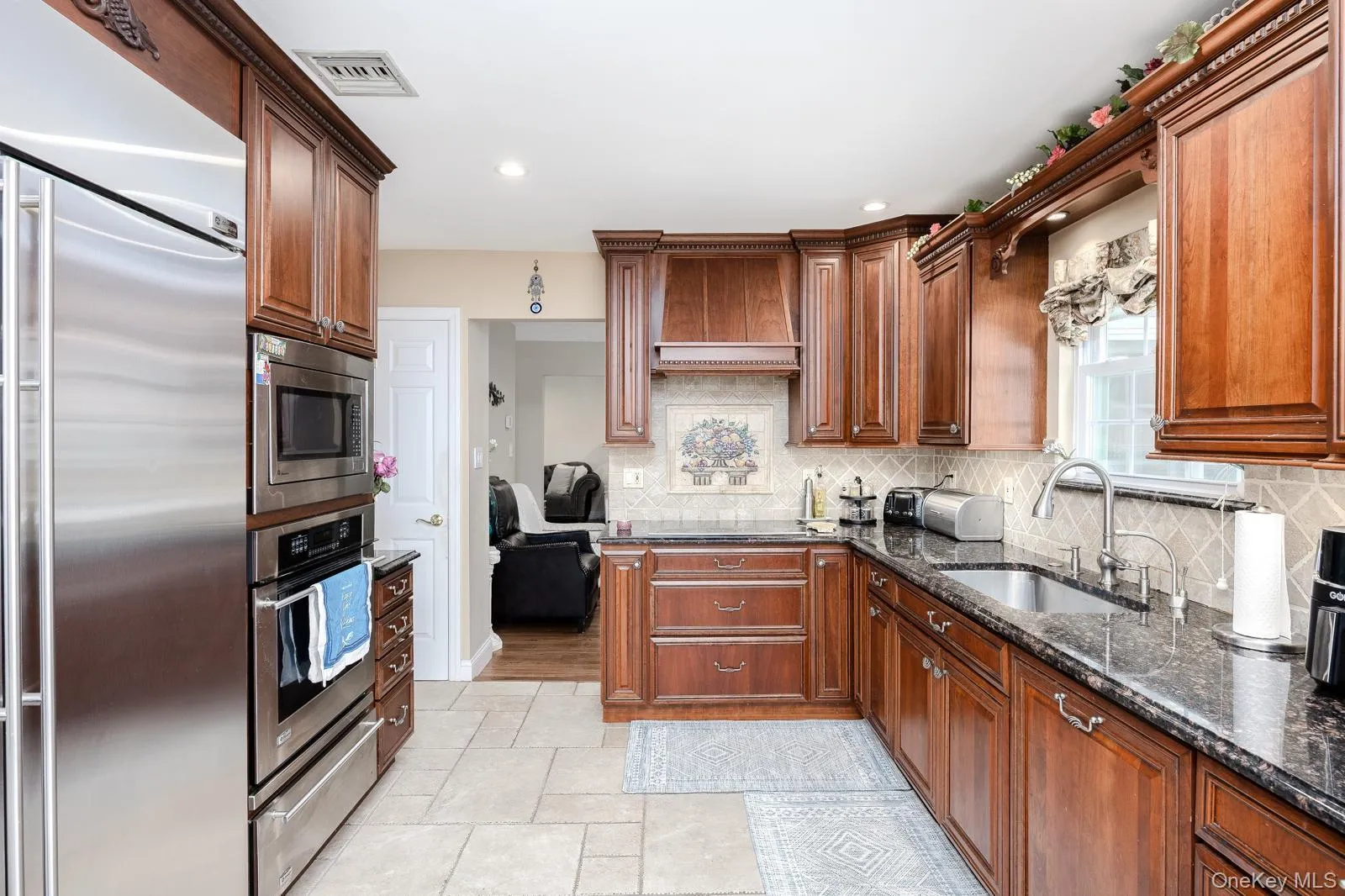 Warm wood cabinetry with crown molding, stainless steel appliances, dark stone countertops, tile backsplash, and a stainless steel sink with a gooseneck faucet Warm wood cabinetry with crown molding, stainless steel appliances, dark stone countertops, tile backsplash, and a stainless steel sink with a gooseneck faucet