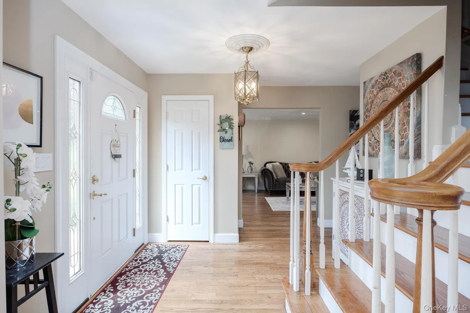 Entryway featuring wood-finish flooring, a white paneled entry door with sidelights, a decorative ceiling medallion with an attached light fixture, and a staircase with wood handrails and white balusters Entryway featuring wood-finish flooring, a white paneled entry door with sidelights, a decorative ceiling medallion with an attached light fixture, and a staircase with wood handrails and white balusters