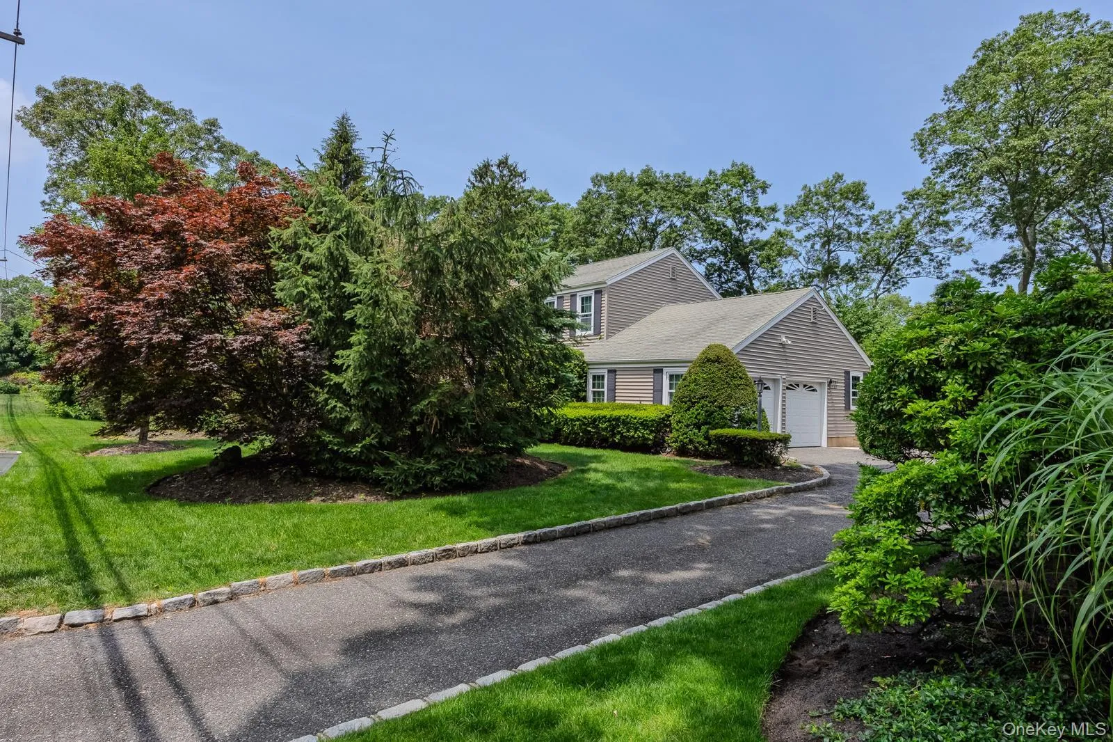Asphalt driveway with stone border, two-car garage, and mature landscaping Asphalt driveway with stone border, two-car garage, and mature landscaping