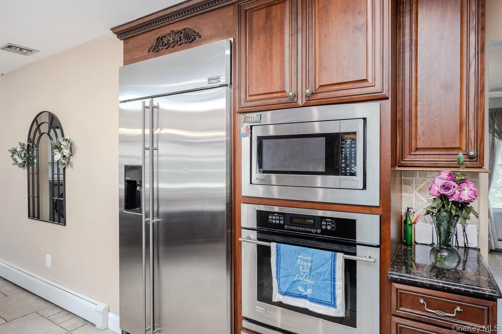 Stainless steel refrigerator, integrated microwave, built-in oven, wood cabinetry, and dark countertop Stainless steel refrigerator, integrated microwave, built-in oven, wood cabinetry, and dark countertop