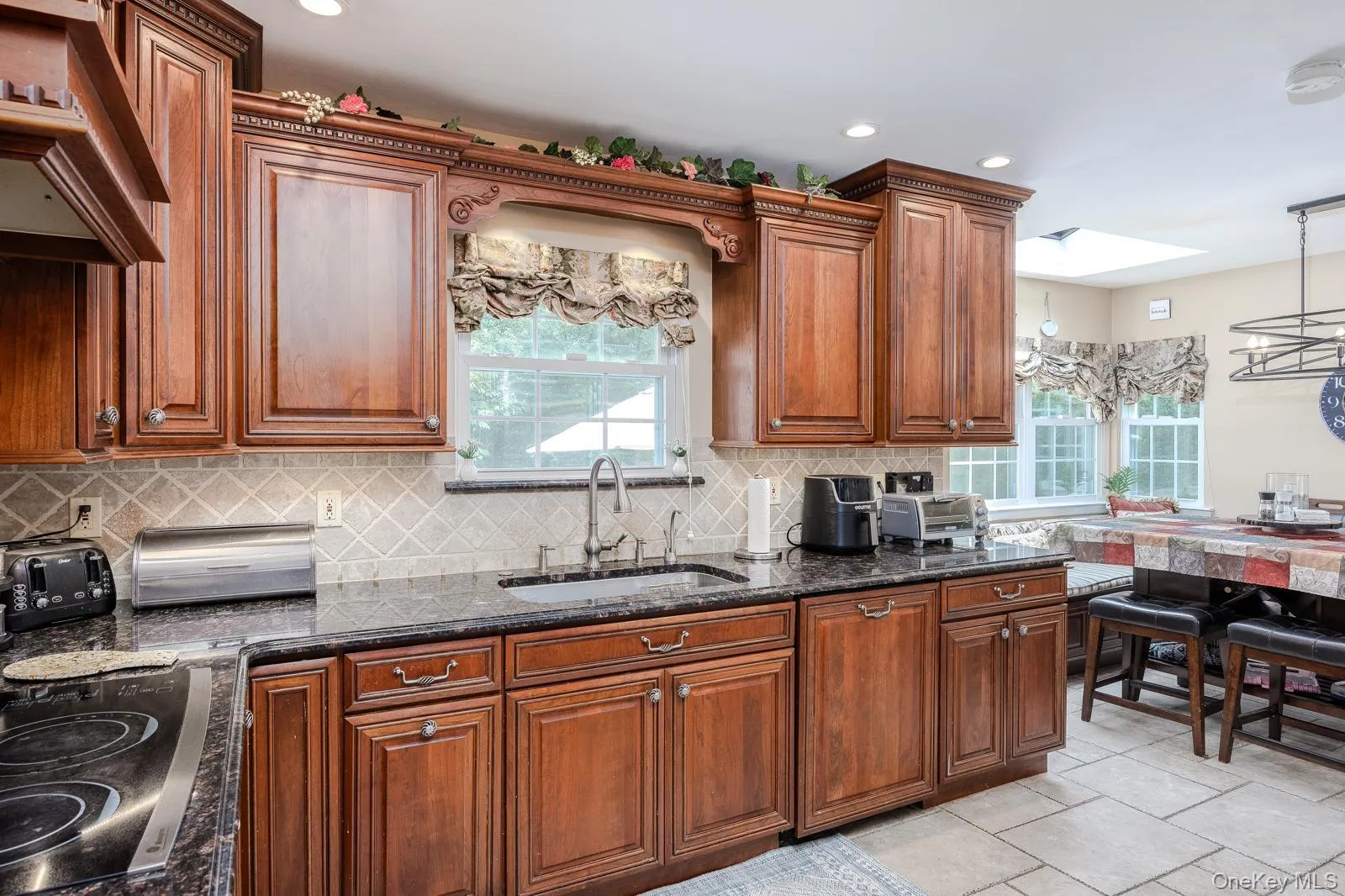 Rich wood cabinetry with decorative molding, dark stone countertops, diamond-patterned tile backsplash, and a contemporary sink faucet Rich wood cabinetry with decorative molding, dark stone countertops, diamond-patterned tile backsplash, and a contemporary sink faucet