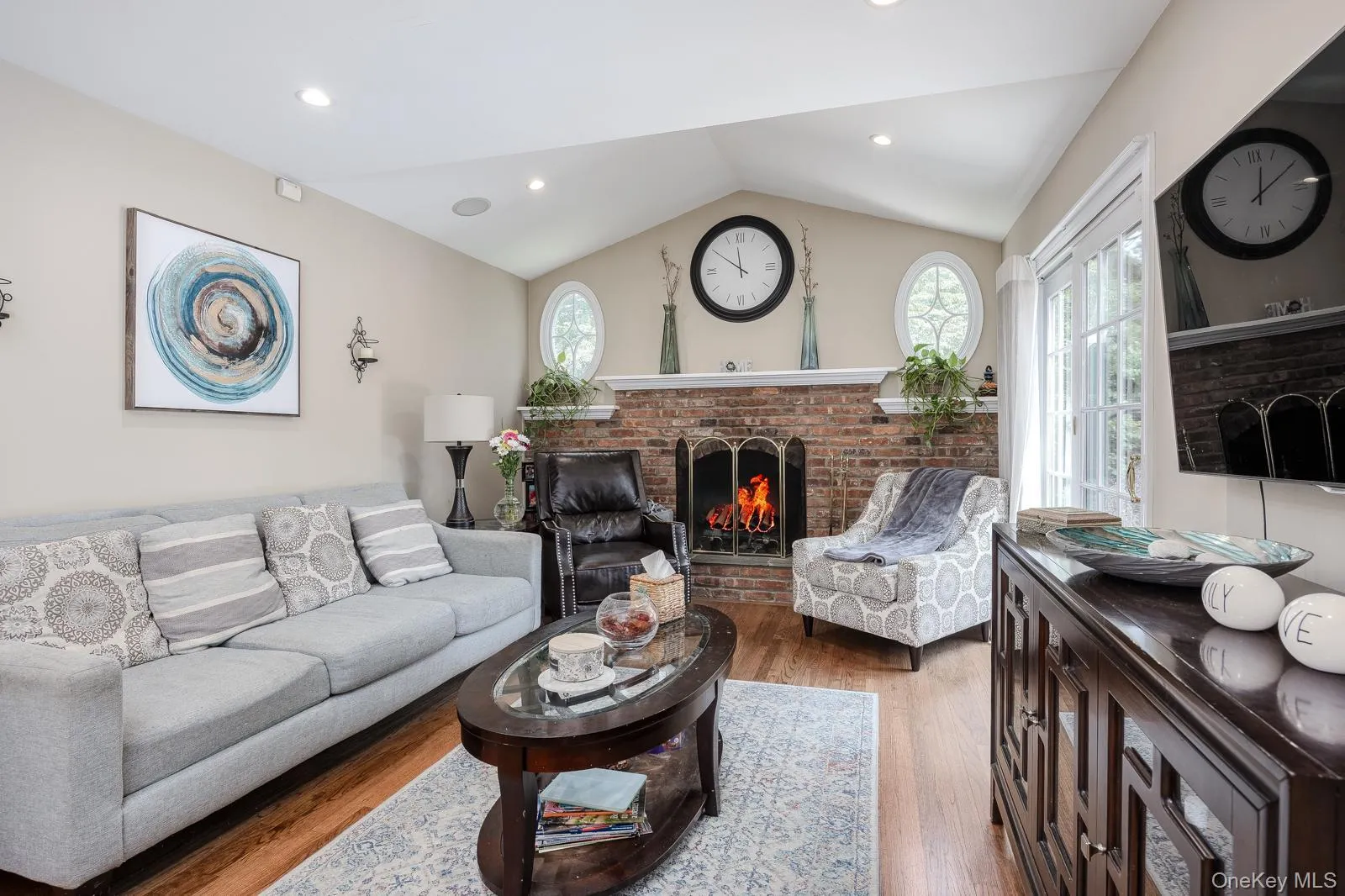 Vaulted ceiling living area featuring hardwood flooring, a brick fireplace, French doors, and recessed lighting Vaulted ceiling living area featuring hardwood flooring, a brick fireplace, French doors, and recessed lighting