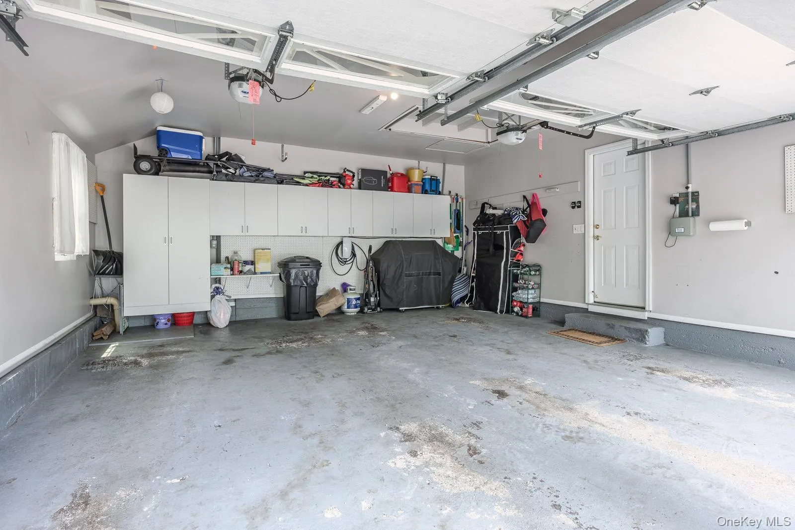Attached garage featuring built-in cabinetry, overhead lighting, and a service door Attached garage featuring built-in cabinetry, overhead lighting, and a service door