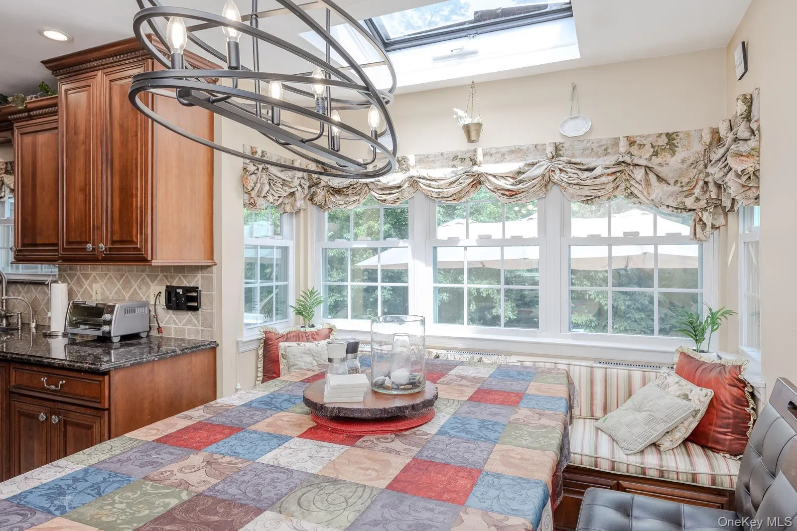 Built-in banquette seating with striped cushions, wood-finish cabinetry, dark stone countertops, skylight, and a decorative overhead light fixture Built-in banquette seating with striped cushions, wood-finish cabinetry, dark stone countertops, skylight, and a decorative overhead light fixture