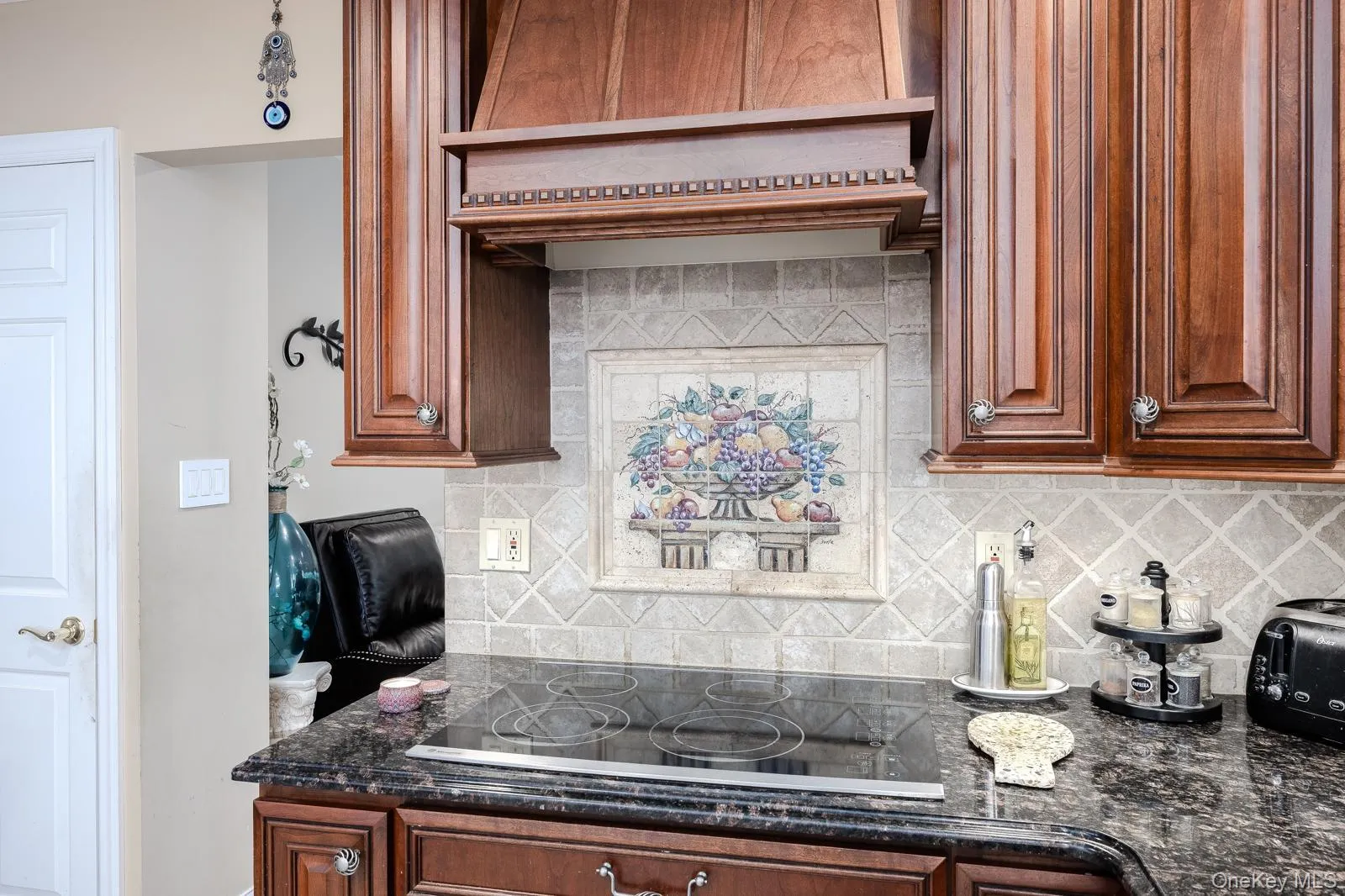 Integrated cooktop with a dark stone countertop, complemented by a decorative tile backsplash and custom wood cabinetry Integrated cooktop with a dark stone countertop, complemented by a decorative tile backsplash and custom wood cabinetry