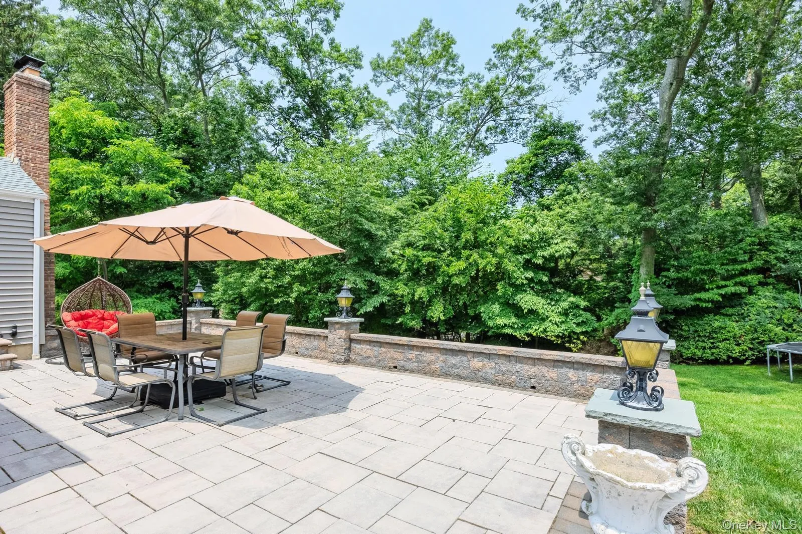Expansive paver patio with a stone retaining wall and lush perimeter landscaping Expansive paver patio with a stone retaining wall and lush perimeter landscaping