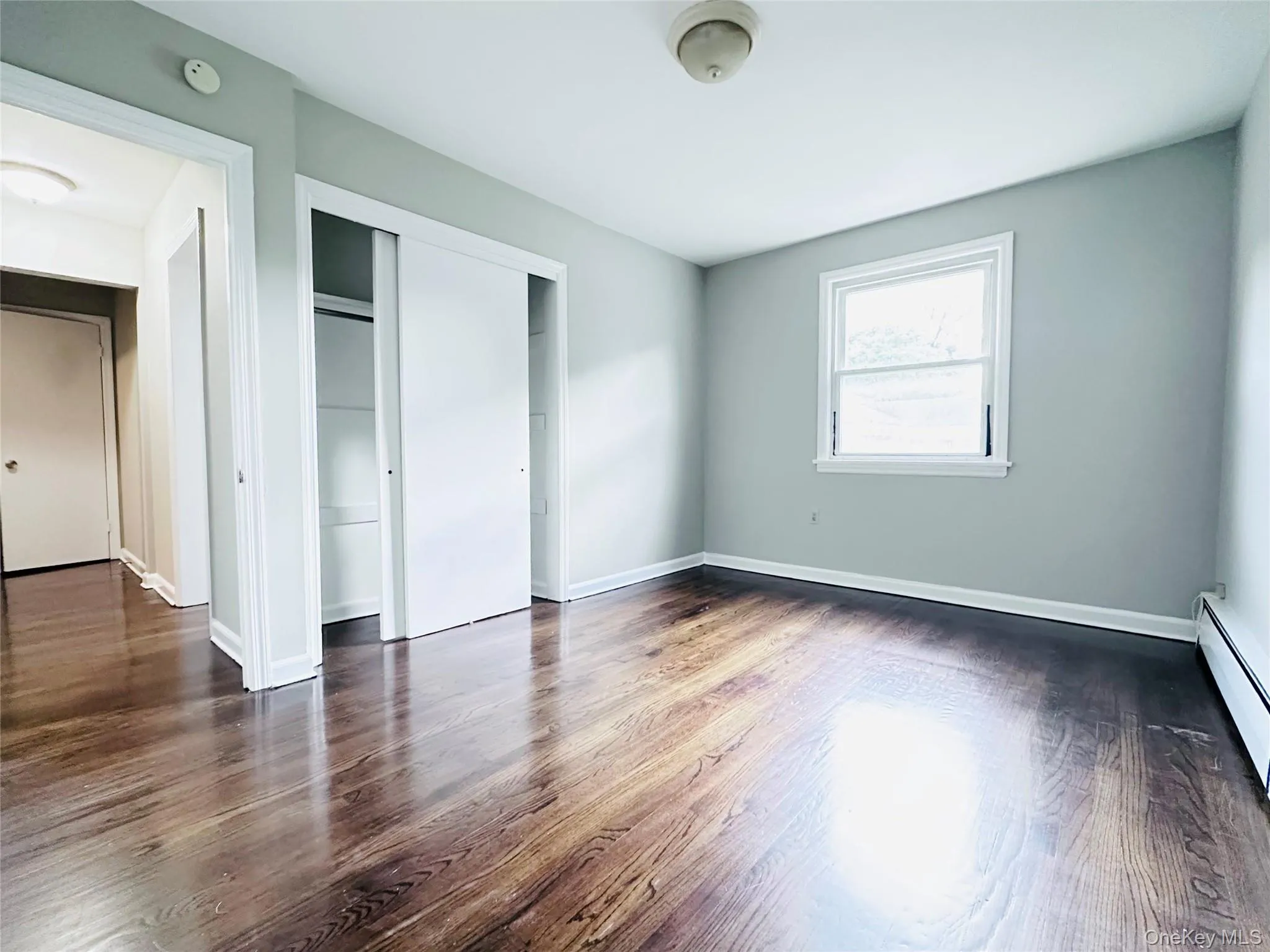 Bedroom 1 featuring wood-finish flooring, natural light, ceiling light fixture and a built-in closet with sliding doors Bedroom 1 featuring wood-finish flooring, natural light, ceiling light fixture and a built-in closet with sliding doors