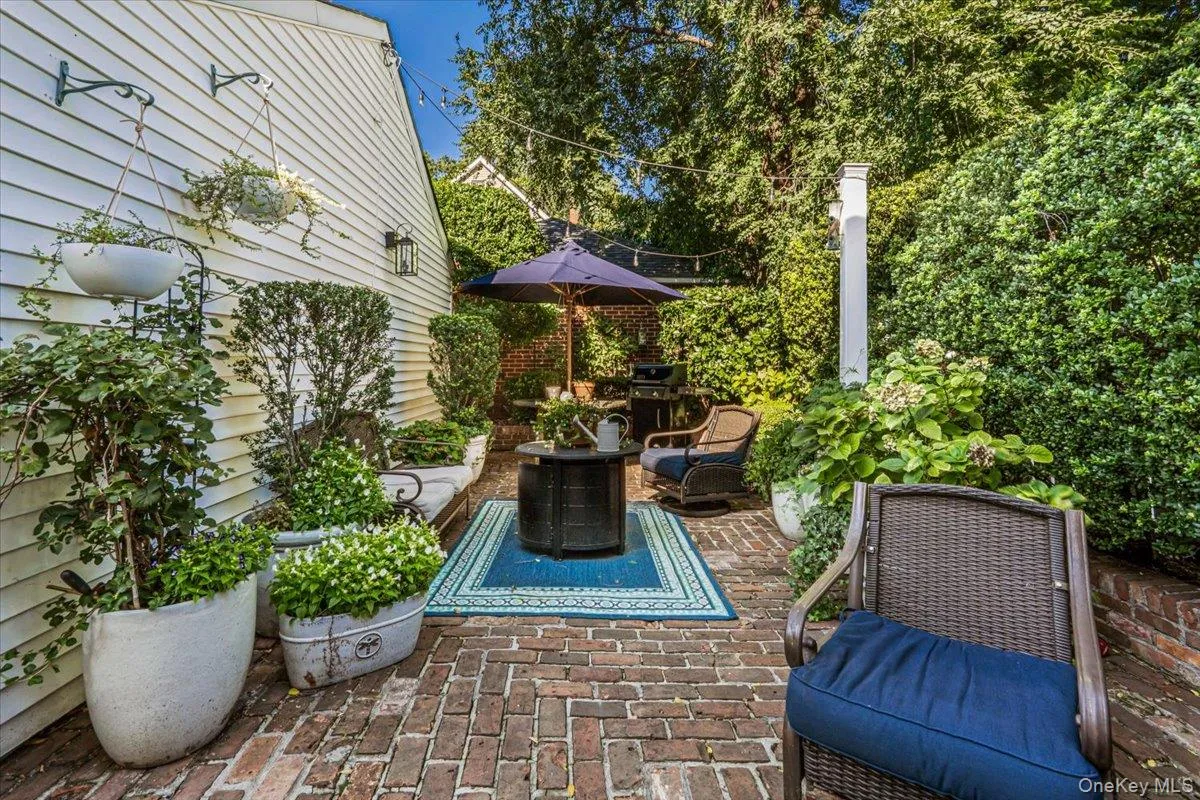Brick paver patio featuring a fire pit, wall-mounted exterior lighting, and abundant perimeter plantings. Brick paver patio featuring a fire pit, wall-mounted exterior lighting, and abundant perimeter plantings.