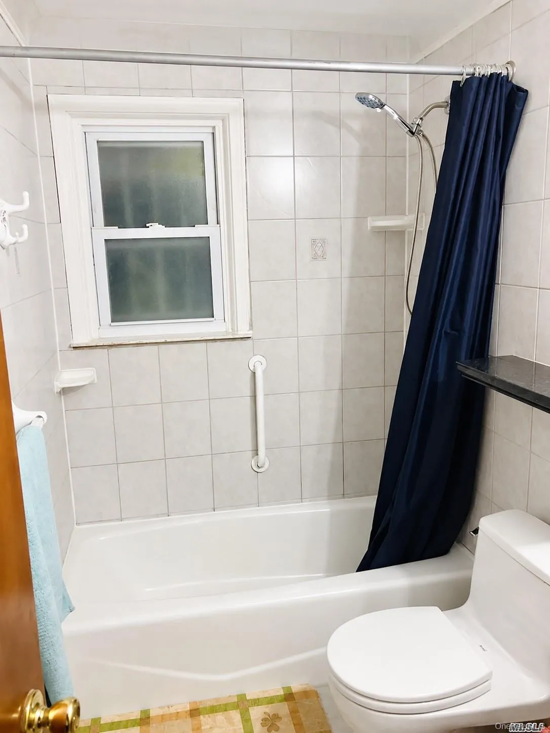 White tiled shower surround with an integrated bathtub, white window, and handheld shower fixture White tiled shower surround with an integrated bathtub, white window, and handheld shower fixture