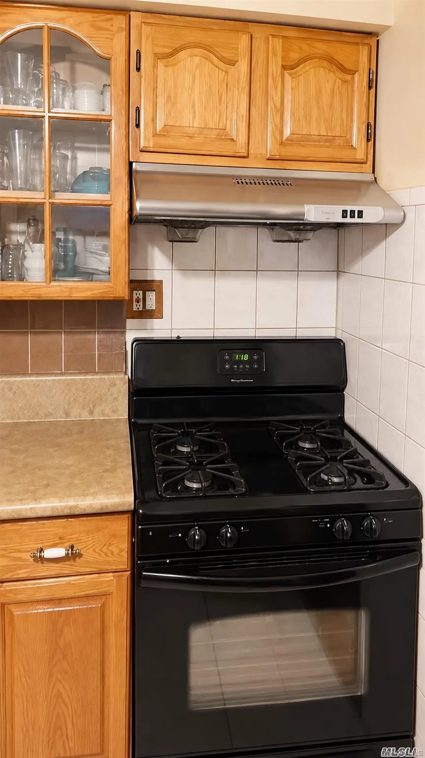 Kitchen featuring a black gas range, stainless steel range hood, wooden cabinetry, and tile backsplash Kitchen featuring a black gas range, stainless steel range hood, wooden cabinetry, and tile backsplash