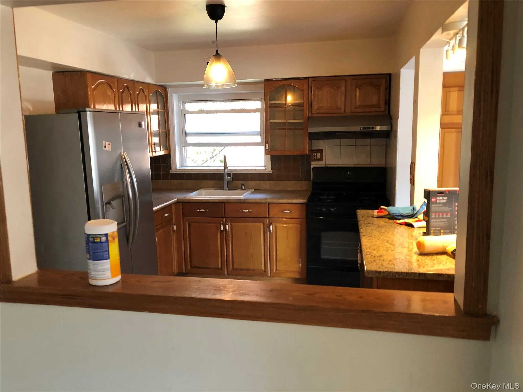 Kitchen with wood cabinetry, stainless steel refrigerator, black range, and speckled countertops Kitchen with wood cabinetry, stainless steel refrigerator, black range, and speckled countertops