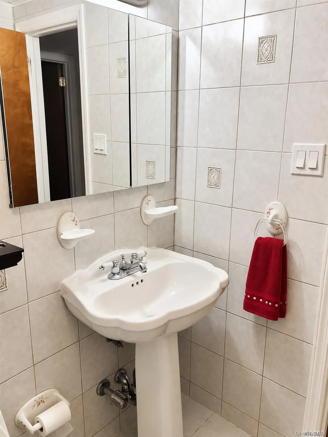 Pedestal sink with chrome faucet, complemented by a mirrored medicine cabinet and tiled walls with decorative accents Pedestal sink with chrome faucet, complemented by a mirrored medicine cabinet and tiled walls with decorative accents