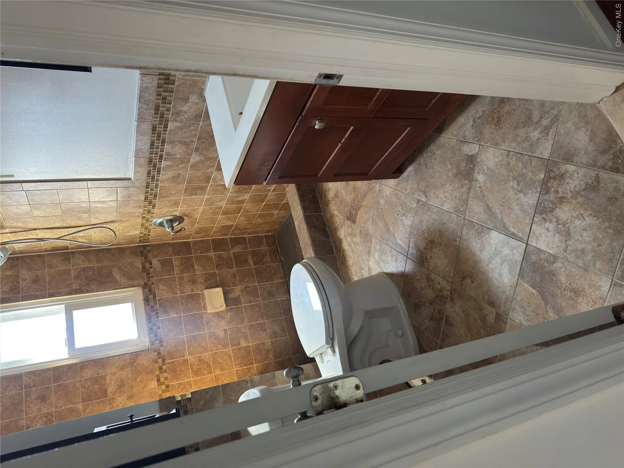 Tiled shower with mosaic accent, single window, floor-mounted toilet, and wood-finish vanity with an integrated sink Tiled shower with mosaic accent, single window, floor-mounted toilet, and wood-finish vanity with an integrated sink