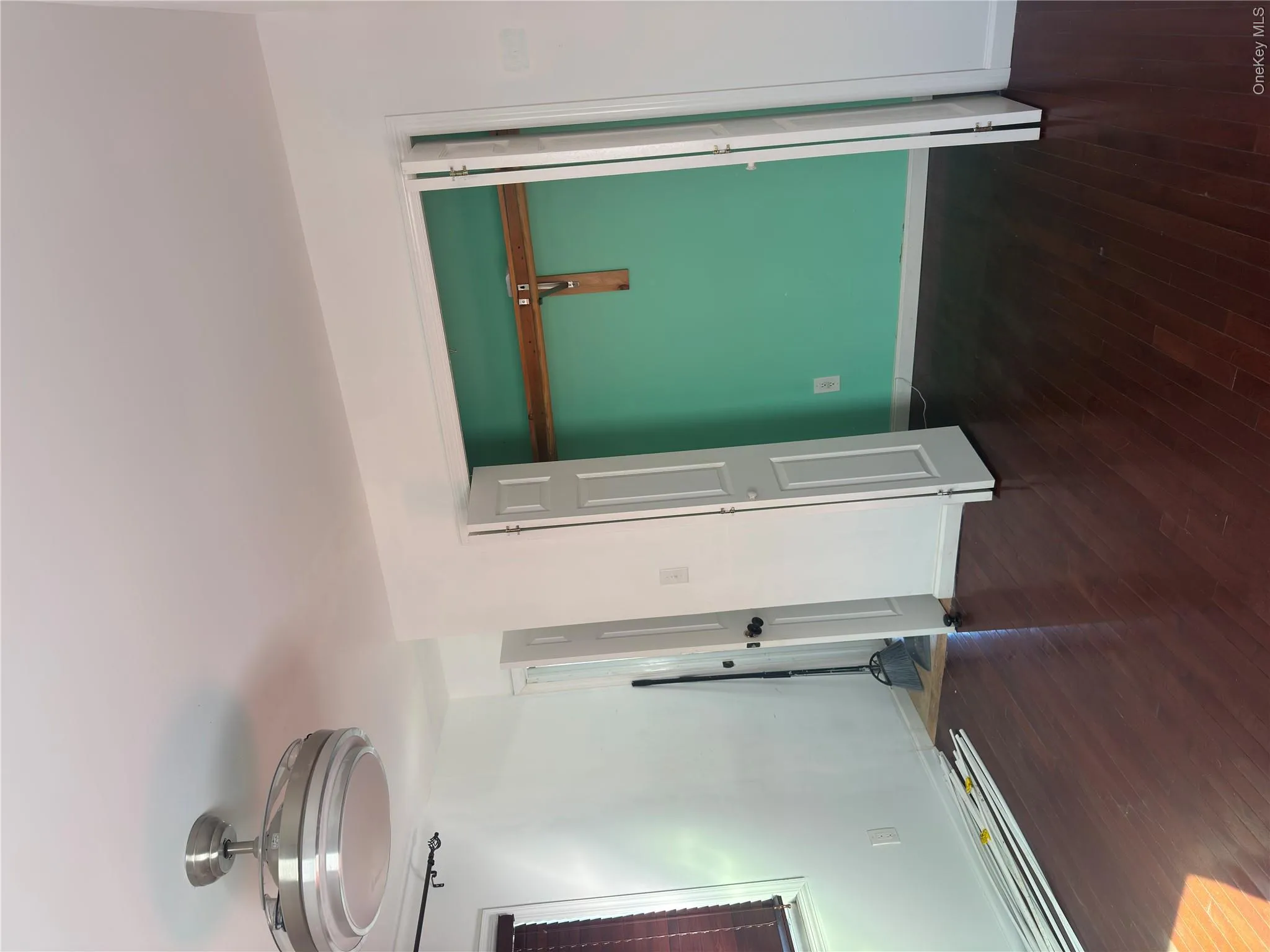 Wood-finish flooring throughout, white walls, ceiling-mounted light fixture, window with horizontal blinds, and a bi-fold door closet with a wooden rod Wood-finish flooring throughout, white walls, ceiling-mounted light fixture, window with horizontal blinds, and a bi-fold door closet with a wooden rod