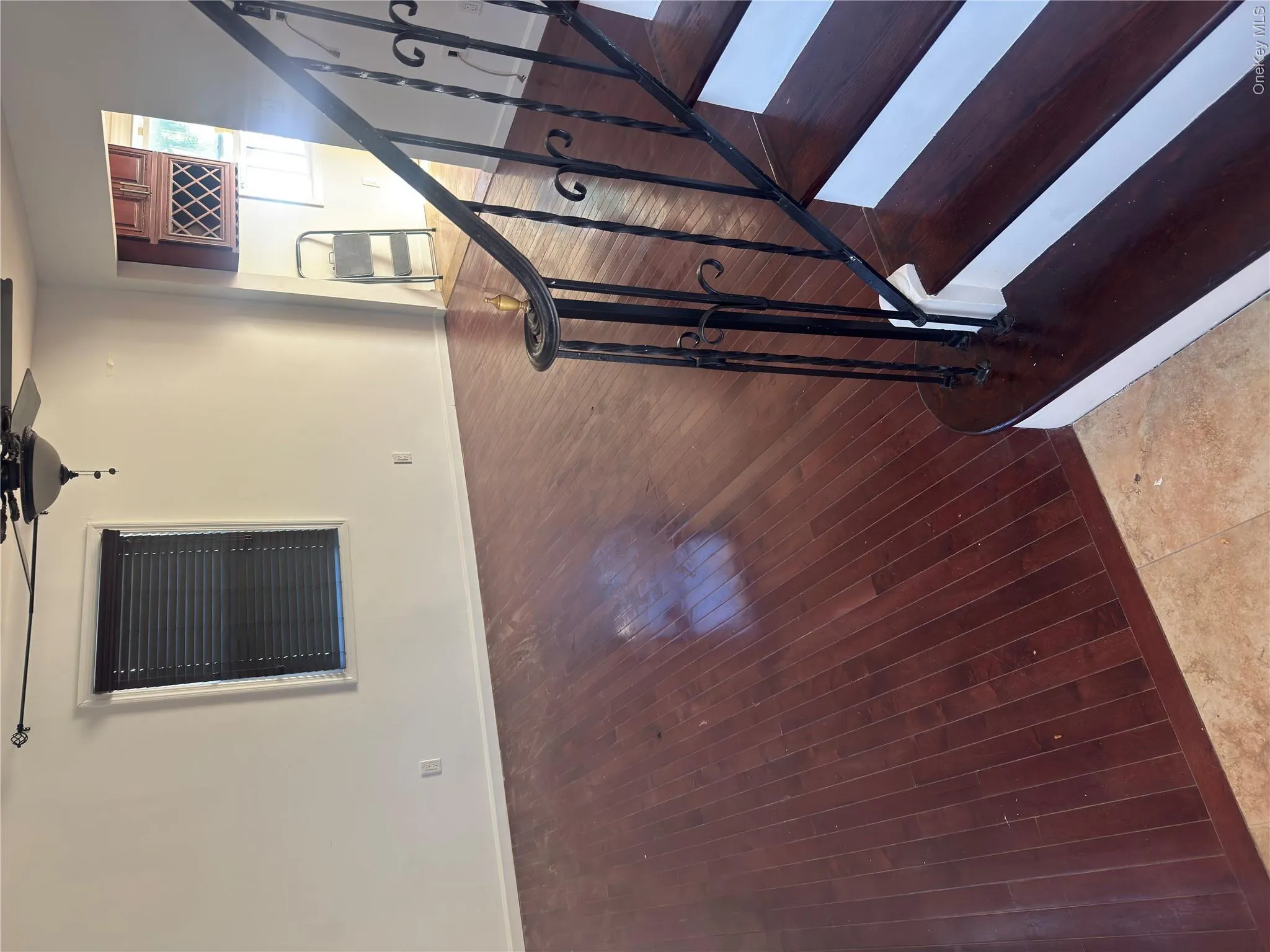 Wood-finish flooring throughout, ceiling fan with light fixture, window with blinds, and staircase with wrought iron railing Wood-finish flooring throughout, ceiling fan with light fixture, window with blinds, and staircase with wrought iron railing