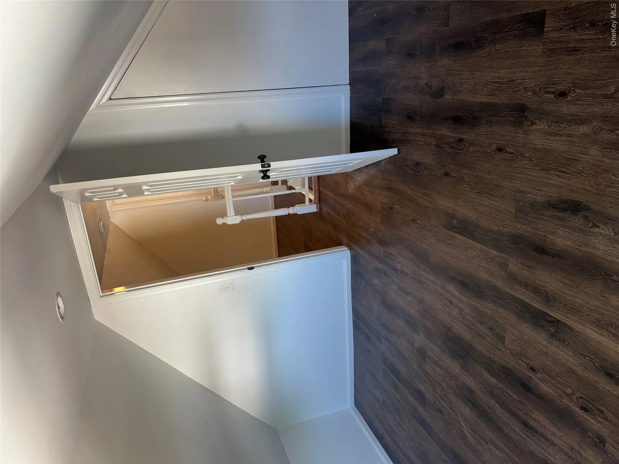 Wood-finish flooring with recessed lighting, angled wall design, and a paneled door Wood-finish flooring with recessed lighting, angled wall design, and a paneled door