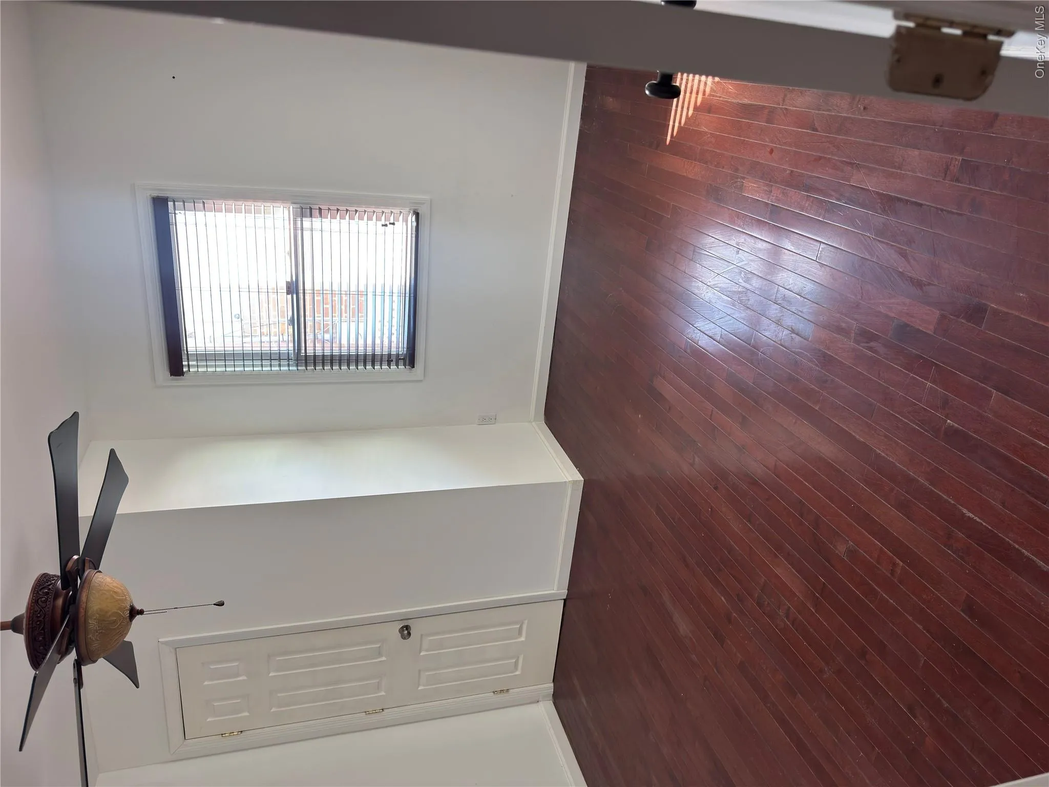 Hardwood flooring, ceiling fan with light fixture, window with blinds, and white paneled door Hardwood flooring, ceiling fan with light fixture, window with blinds, and white paneled door