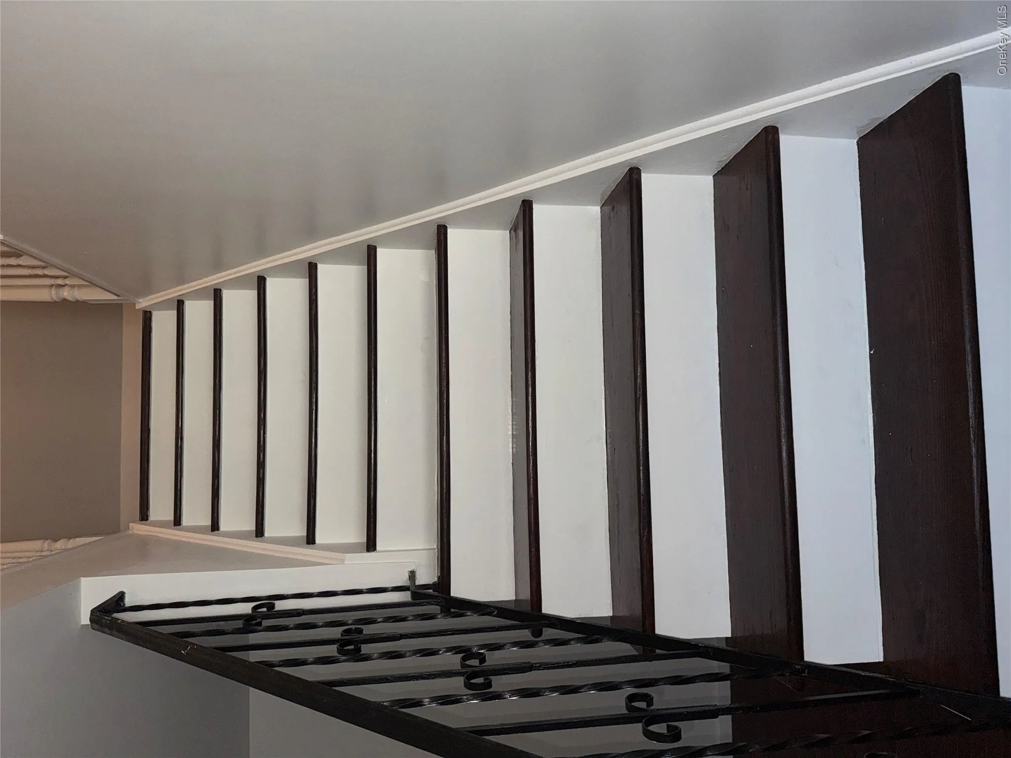 Staircase featuring dark wood-finish treads, white risers, and a wrought iron handrail Staircase featuring dark wood-finish treads, white risers, and a wrought iron handrail