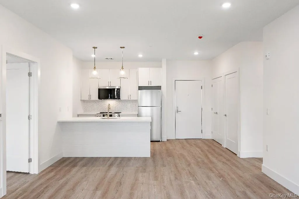 Kitchen with tasteful backsplash, kitchen peninsula, pendant lighting, white cabinets, and appliances with stainless steel finishes Kitchen with tasteful backsplash, kitchen peninsula, pendant lighting, white cabinets, and appliances with stainless steel finishes