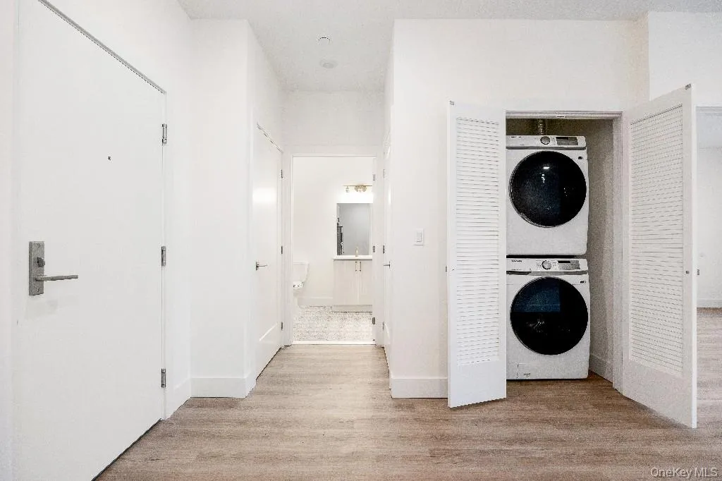 Washroom with light hardwood / wood-style flooring and stacked washer and clothes dryer Washroom with light hardwood / wood-style flooring and stacked washer and clothes dryer