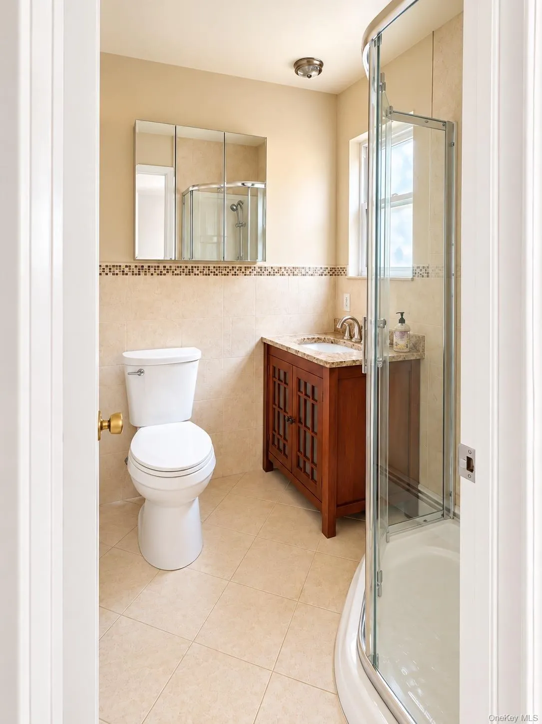 Tiled bathroom featuring a curved glass shower enclosure, wood-finish vanity with a stone countertop, and a mirrored medicine cabinet Tiled bathroom featuring a curved glass shower enclosure, wood-finish vanity with a stone countertop, and a mirrored medicine cabinet