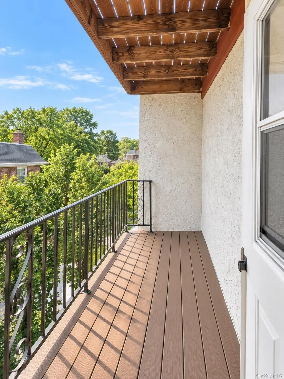Balcony featuring composite decking, decorative iron railing, a textured stucco exterior wall, and a wood slat ceiling Balcony featuring composite decking, decorative iron railing, a textured stucco exterior wall, and a wood slat ceiling