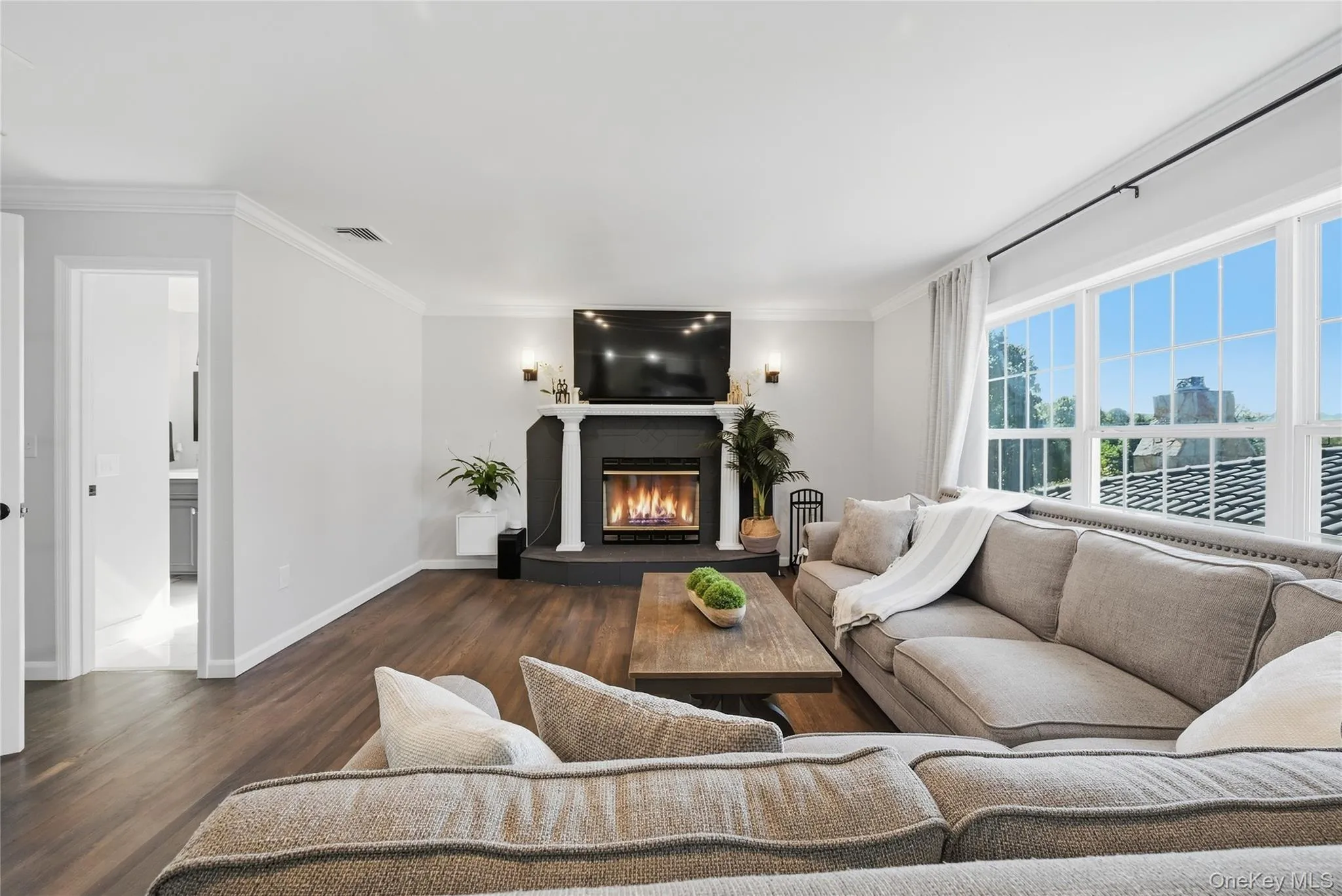 Living area featuring wood-finish flooring, a contemporary fireplace with a dark mantel, large multi-pane windows, and recessed lighting Living area featuring wood-finish flooring, a contemporary fireplace with a dark mantel, large multi-pane windows, and recessed lighting