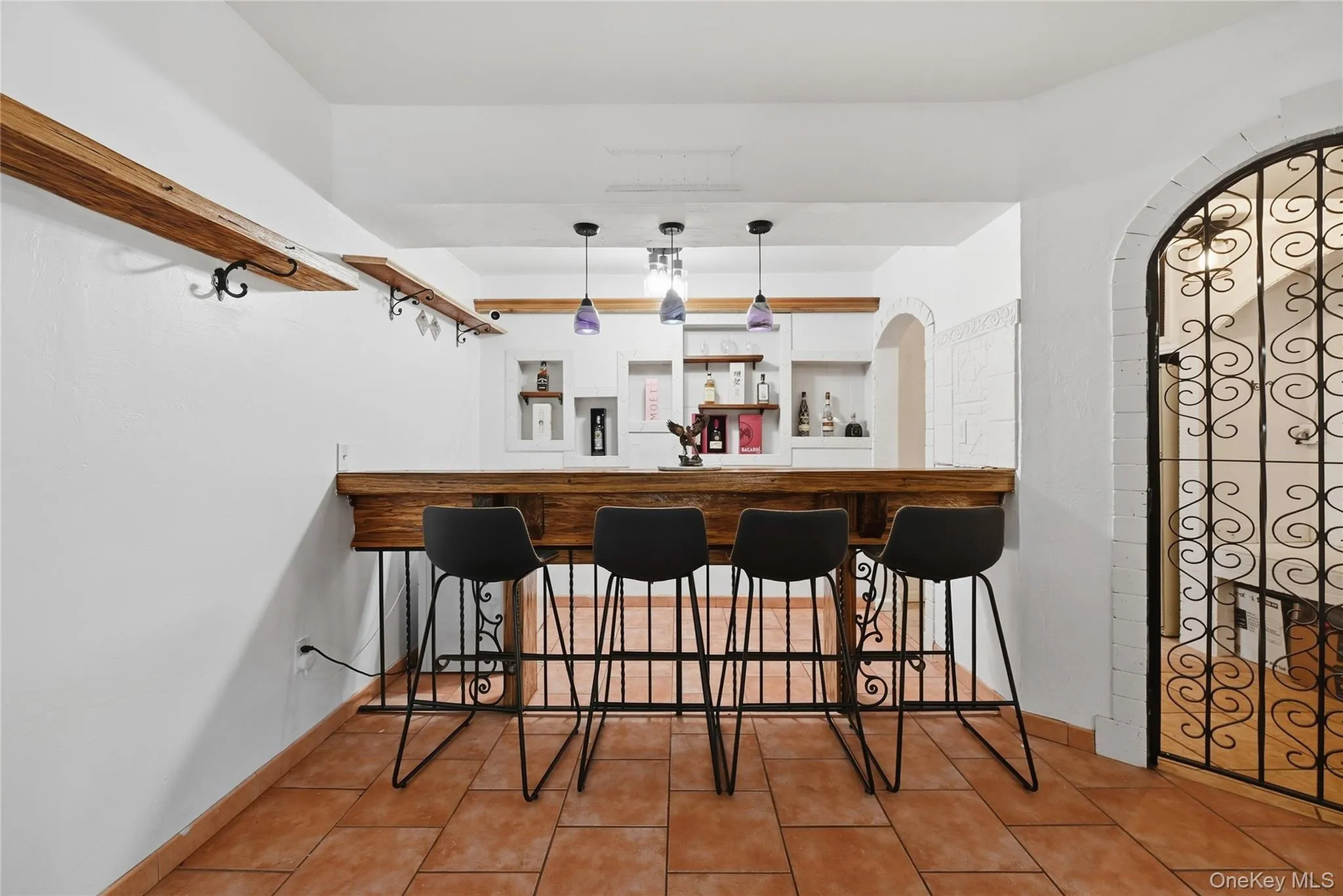 Built-in bar with a substantial wood-finish countertop, decorative ironwork, recessed shelving, and a tiled floor Built-in bar with a substantial wood-finish countertop, decorative ironwork, recessed shelving, and a tiled floor
