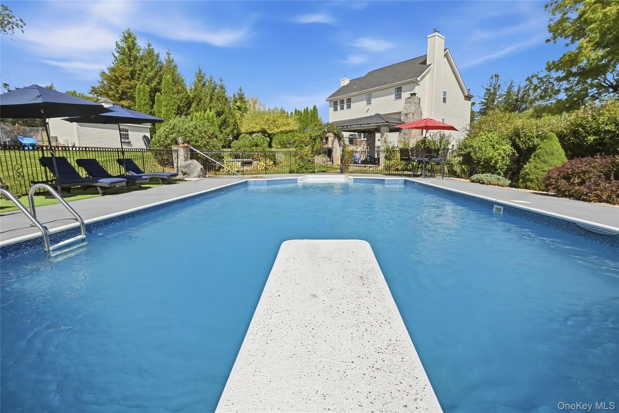 In-ground swimming pool with diving board, surrounded by concrete decking and lush perimeter landscaping In-ground swimming pool with diving board, surrounded by concrete decking and lush perimeter landscaping