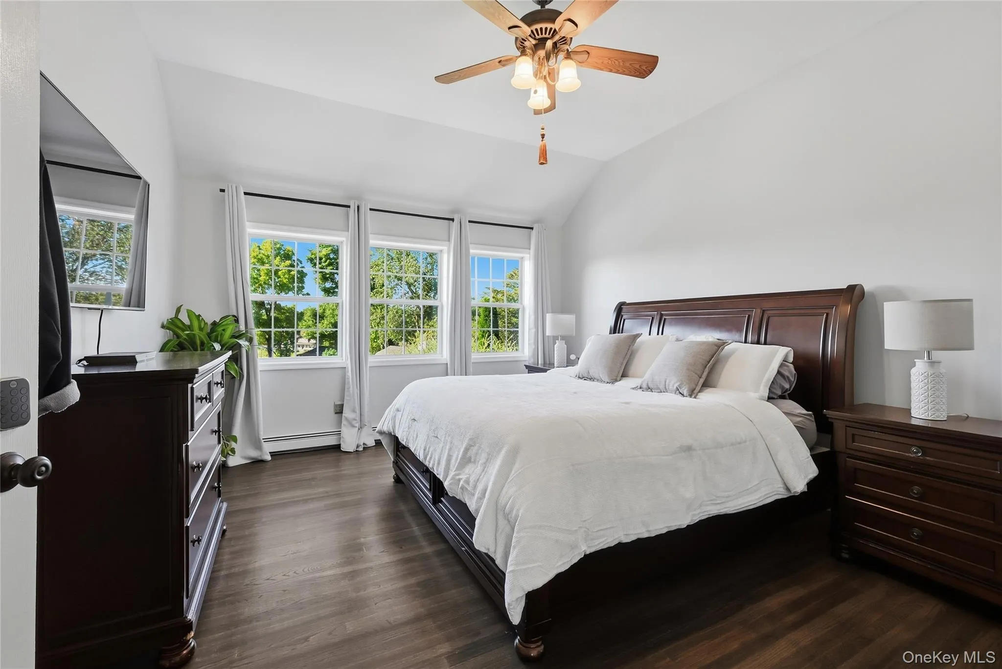 Vaulted ceiling with a ceiling fan, three large windows with white trim, dark wood-finish flooring, and white painted walls Vaulted ceiling with a ceiling fan, three large windows with white trim, dark wood-finish flooring, and white painted walls