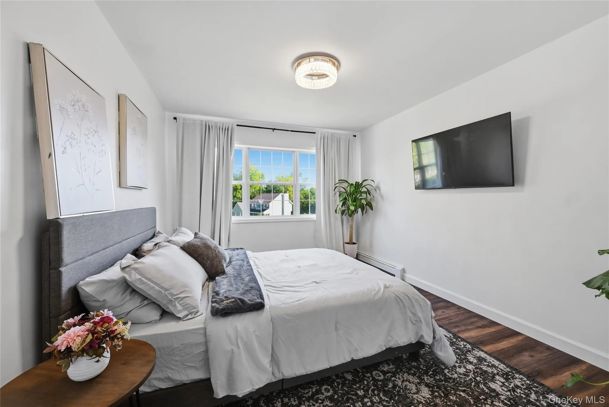 Bright room with wood-finish flooring, a large window, and a ceiling-mounted light fixture Bright room with wood-finish flooring, a large window, and a ceiling-mounted light fixture