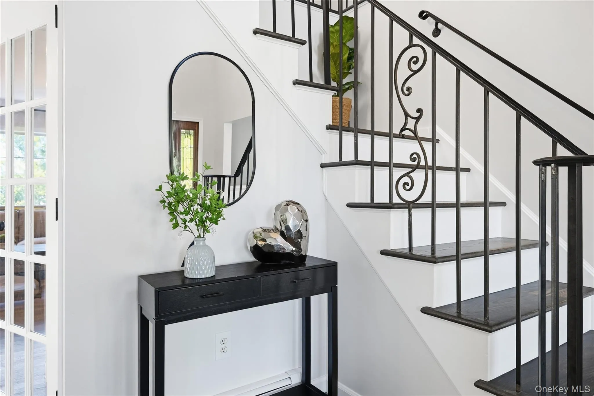 Wrought iron railing with decorative scrollwork, wood-finish stair treads, white risers, and a contemporary arched mirror Wrought iron railing with decorative scrollwork, wood-finish stair treads, white risers, and a contemporary arched mirror