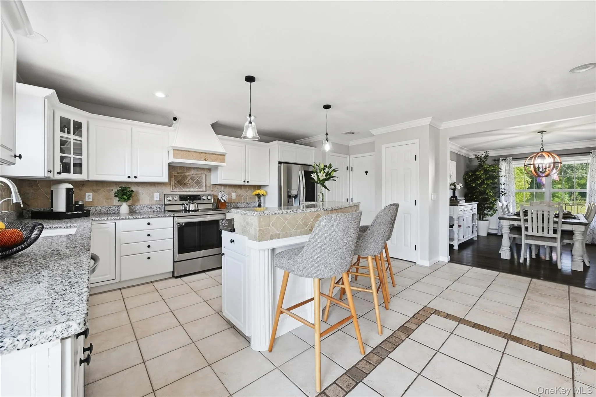 White shaker cabinetry, stainless steel appliances, granite countertops, tile flooring, and a kitchen island with seating White shaker cabinetry, stainless steel appliances, granite countertops, tile flooring, and a kitchen island with seating