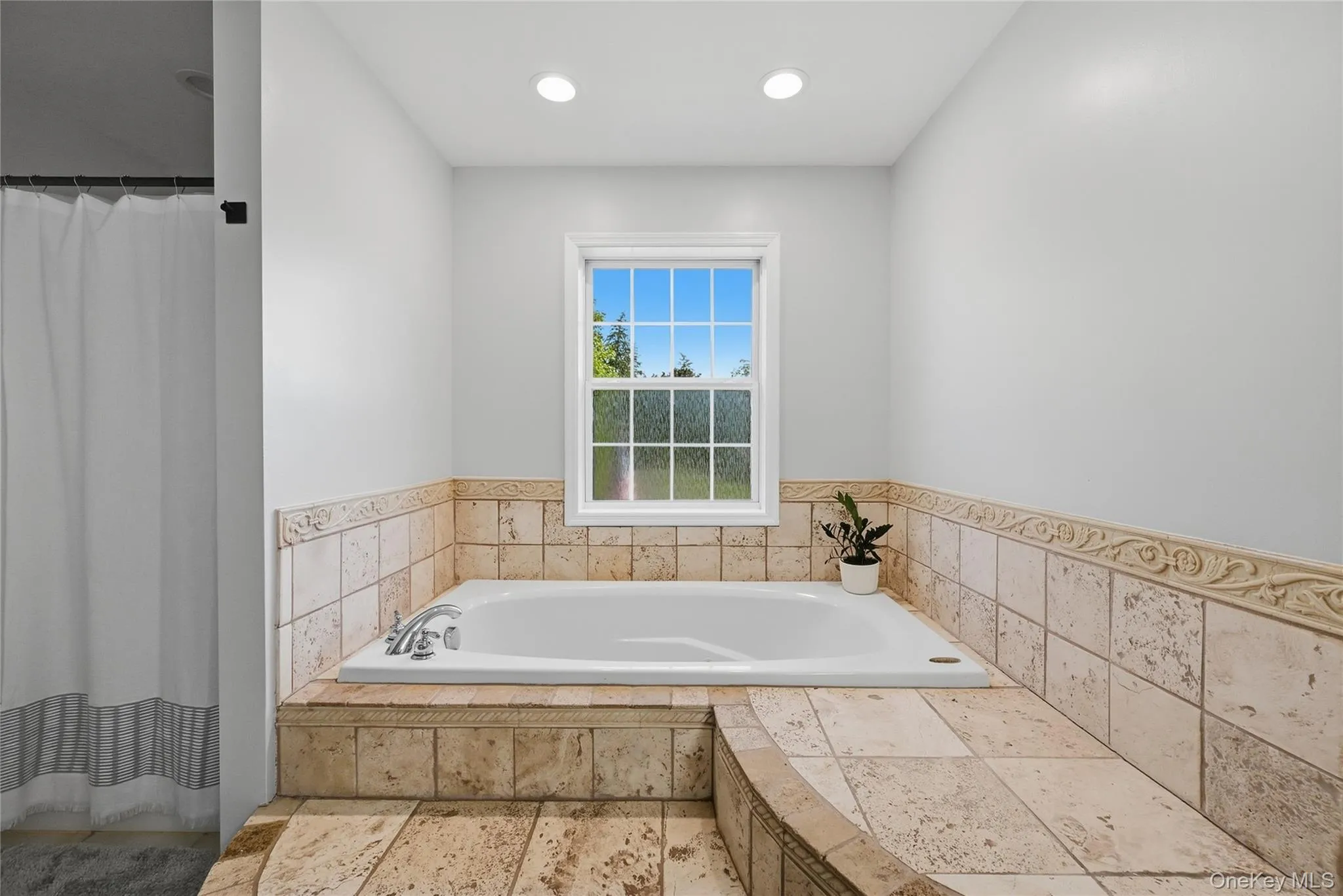 Soaking tub with chrome fixtures, surrounded by stone tile and decorative trim Soaking tub with chrome fixtures, surrounded by stone tile and decorative trim