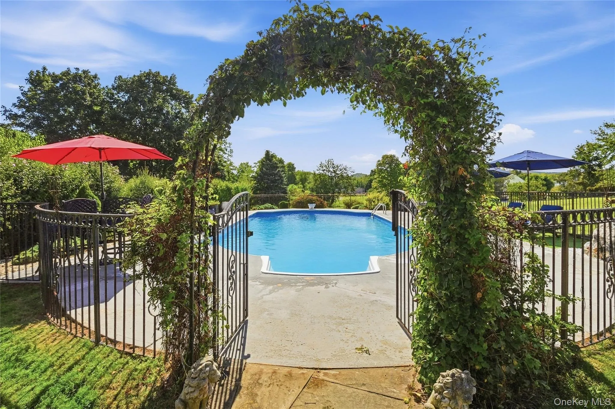 In-ground swimming pool, decorative wrought iron fencing, arched botanical entryway, concrete patio, and lush surrounding foliage In-ground swimming pool, decorative wrought iron fencing, arched botanical entryway, concrete patio, and lush surrounding foliage