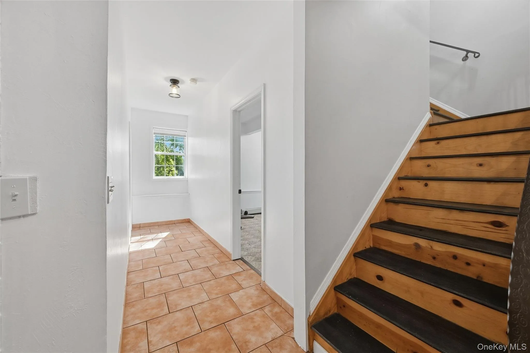 Wood-finish staircase with a dark handrail, tiled flooring, and a window providing natural light Wood-finish staircase with a dark handrail, tiled flooring, and a window providing natural light