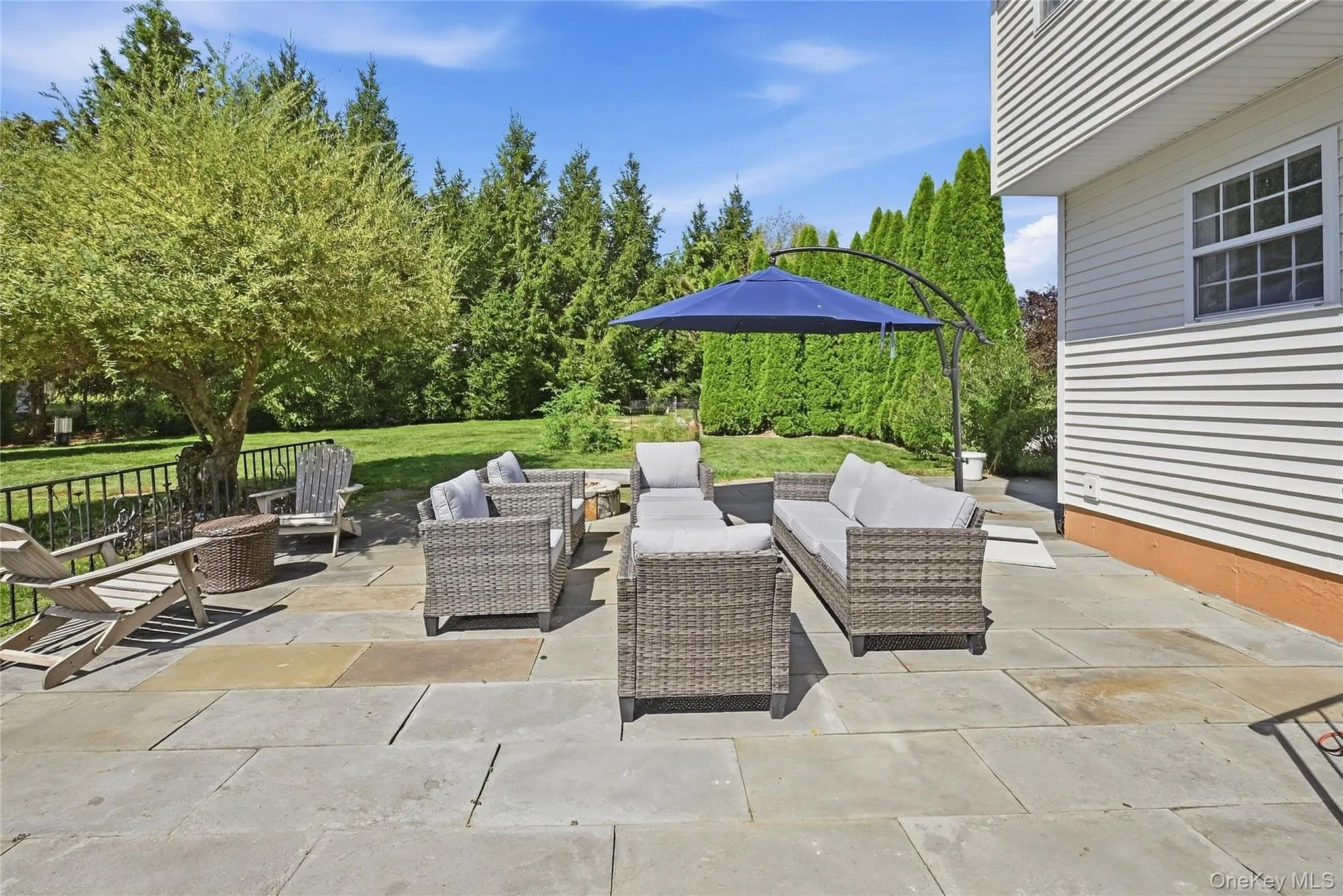 Expansive paver patio with a lush green lawn, mature trees, and a black wrought-iron fence Expansive paver patio with a lush green lawn, mature trees, and a black wrought-iron fence