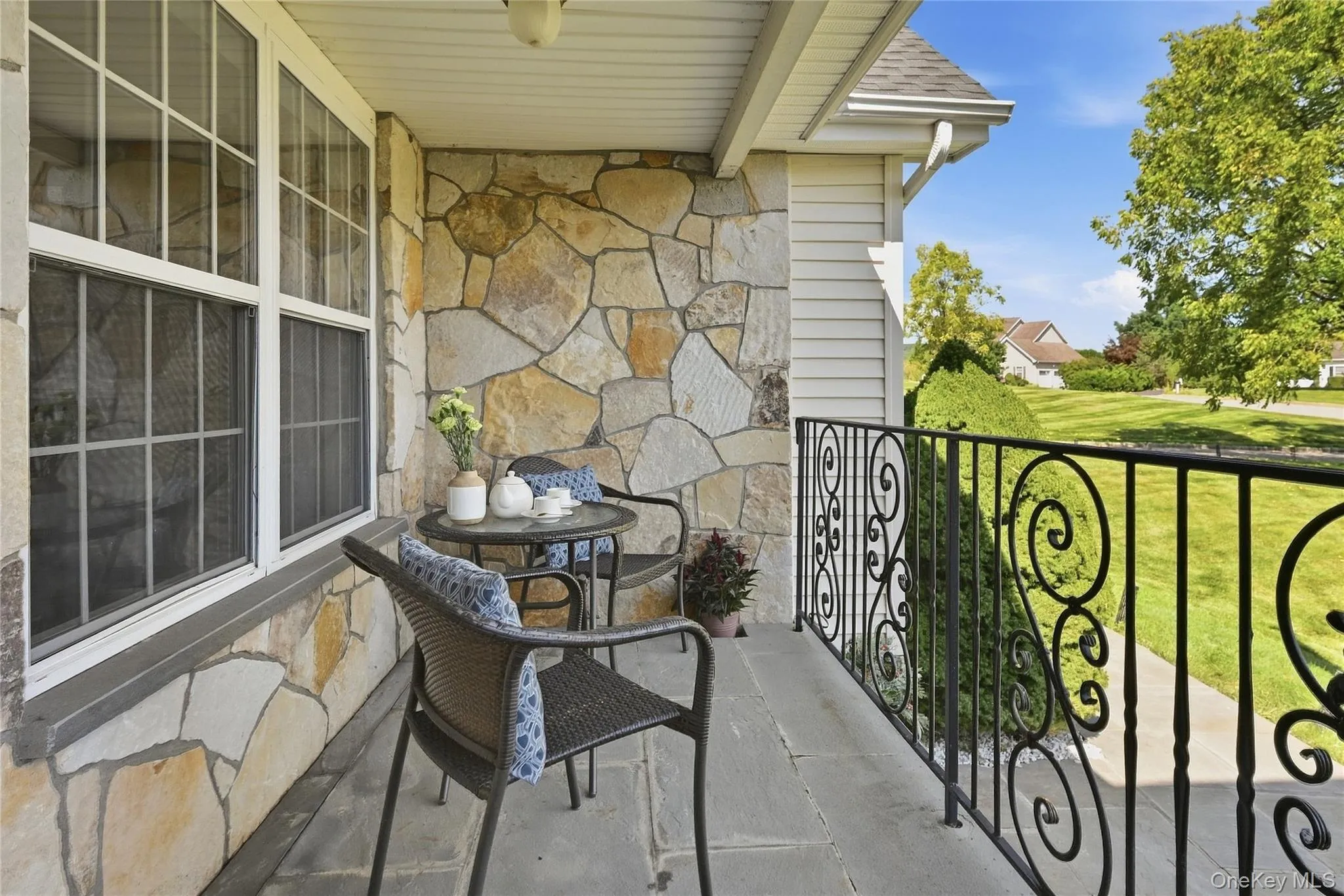 Covered porch featuring natural stone siding, white grid windows, and a black wrought iron railing with scrollwork Covered porch featuring natural stone siding, white grid windows, and a black wrought iron railing with scrollwork