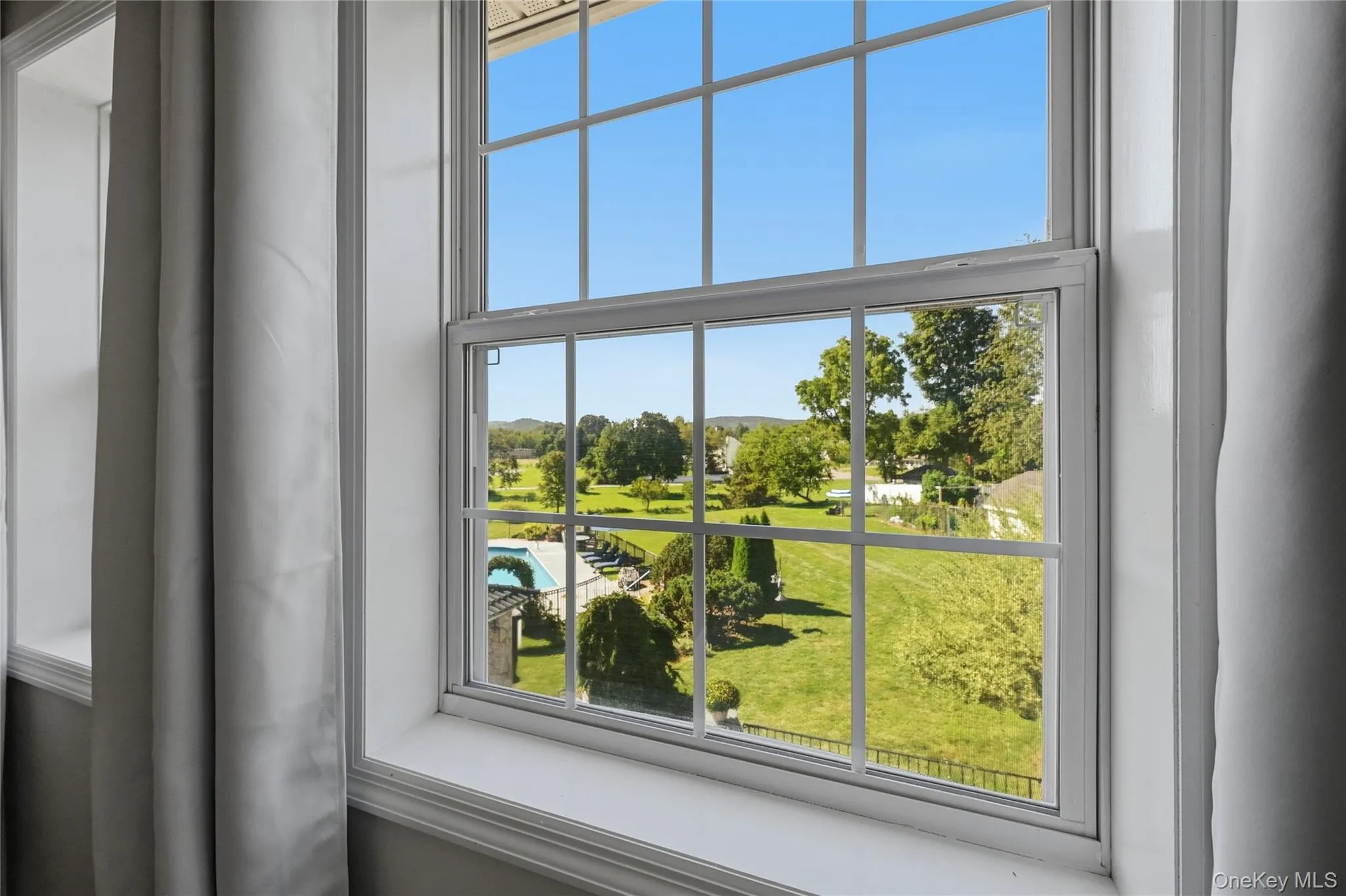 White-framed window with muntins overlooking a sprawling green landscape White-framed window with muntins overlooking a sprawling green landscape