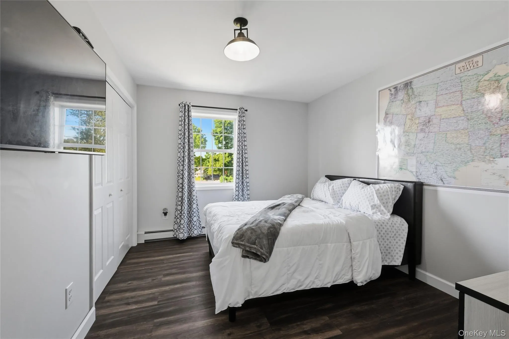 Well-lit room featuring a window with natural light, dark wood-finish flooring, and a white bi-fold closet Well-lit room featuring a window with natural light, dark wood-finish flooring, and a white bi-fold closet