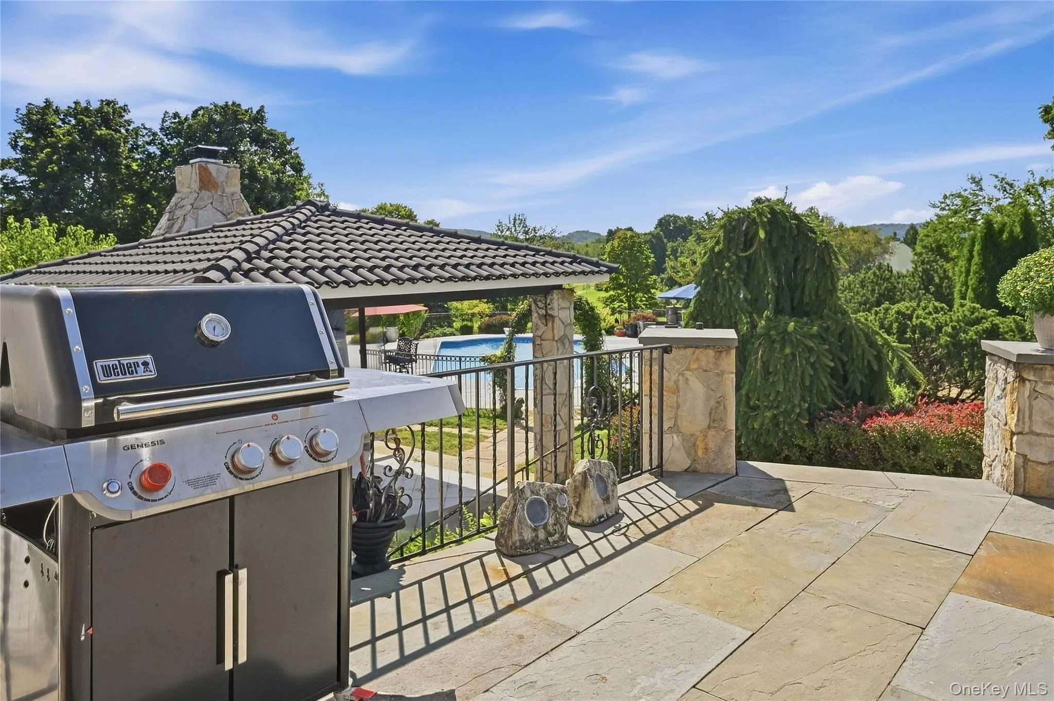 Stone patio with wrought iron railing, leading to a tiled gazebo and a fenced swimming pool Stone patio with wrought iron railing, leading to a tiled gazebo and a fenced swimming pool