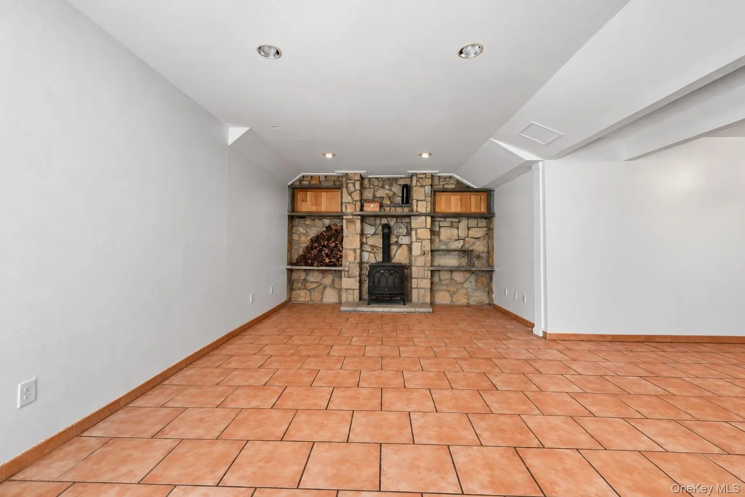 Terracotta-style floor tiling throughout, stone accent wall with built-in wood-burning stove, recessed lighting, and built-in wood cabinetry Terracotta-style floor tiling throughout, stone accent wall with built-in wood-burning stove, recessed lighting, and built-in wood cabinetry